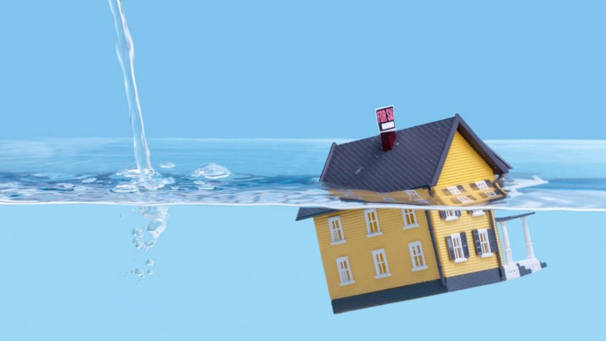 Een geel maquettehuisje met een rood bordje op de schoorsteen zakt weg in helderblauw water.