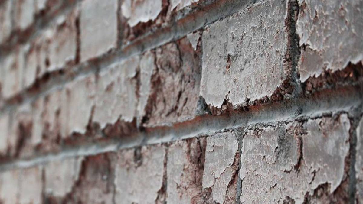 Verweerde bakstenen buitenmuur van dichtbij, met afbrokkelende steenkoppen en grijze mortelvoegen.