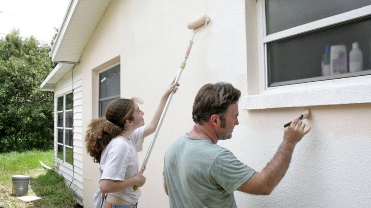 Twee schilders brengen verf aan op de gevel van een woning.